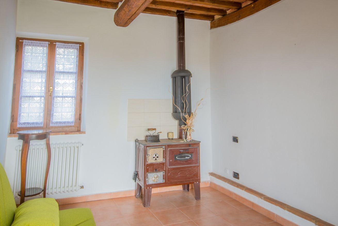 A living room with a wooden ceiling, a radiator, a window with lace curtains, a green sofa, and a vintage stove.