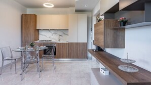 Une cuisine moderne dotée d’un plan de travail en marbre, de meubles en bois et d’un coin repas avec des chaises transparentes.
