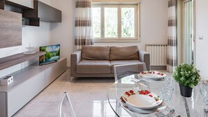 Un salon moderne avec un canapé, un téléviseur et une table à manger, cette dernière étant dressée avec des assiettes et des verres.