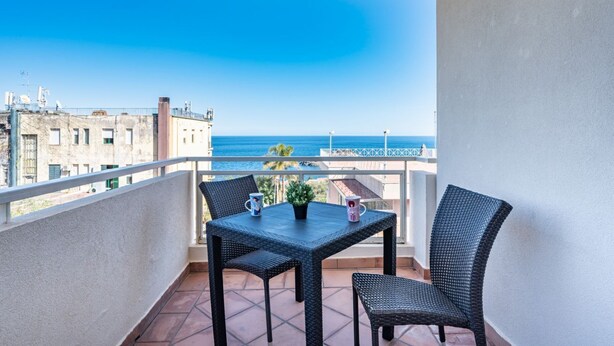 Un balcon avec une table et des chaises, une plante en pot et une vue sur la mer.
