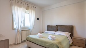 Une chambre à coucher avec un lit, une table de chevet, une fenêtre avec des rideaux et un radiateur.