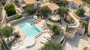 An aerial view of a resort with multiple villas, a central swimming pool, and outdoor seating areas.