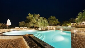 A swimming pool with a stone border, surrounded by trees and a stone wall.
