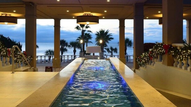 A pool area with a view of the ocean, palm trees, and a covered walkway with railings.