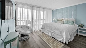 A bedroom with a bed, a chair, a TV, and a window with curtains.