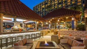 An outdoor bar area with seating, a pool, and a building with multiple balconies in the background.