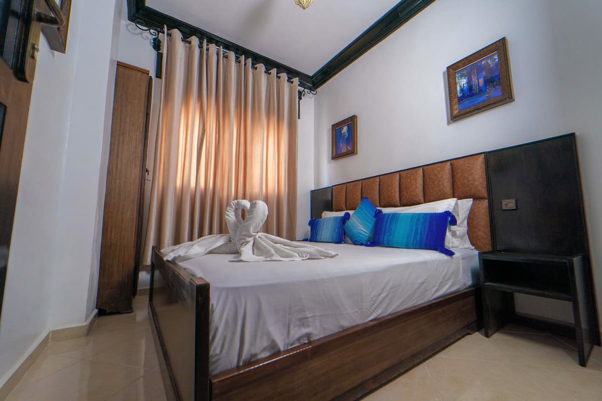 Una habitación de hotel con una cama grande, cabecera de madera, una mesita de noche y un cuadro en la pared.