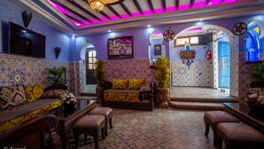 Un intérieur de style marocain avec un canapé, un pouf et un téléviseur.