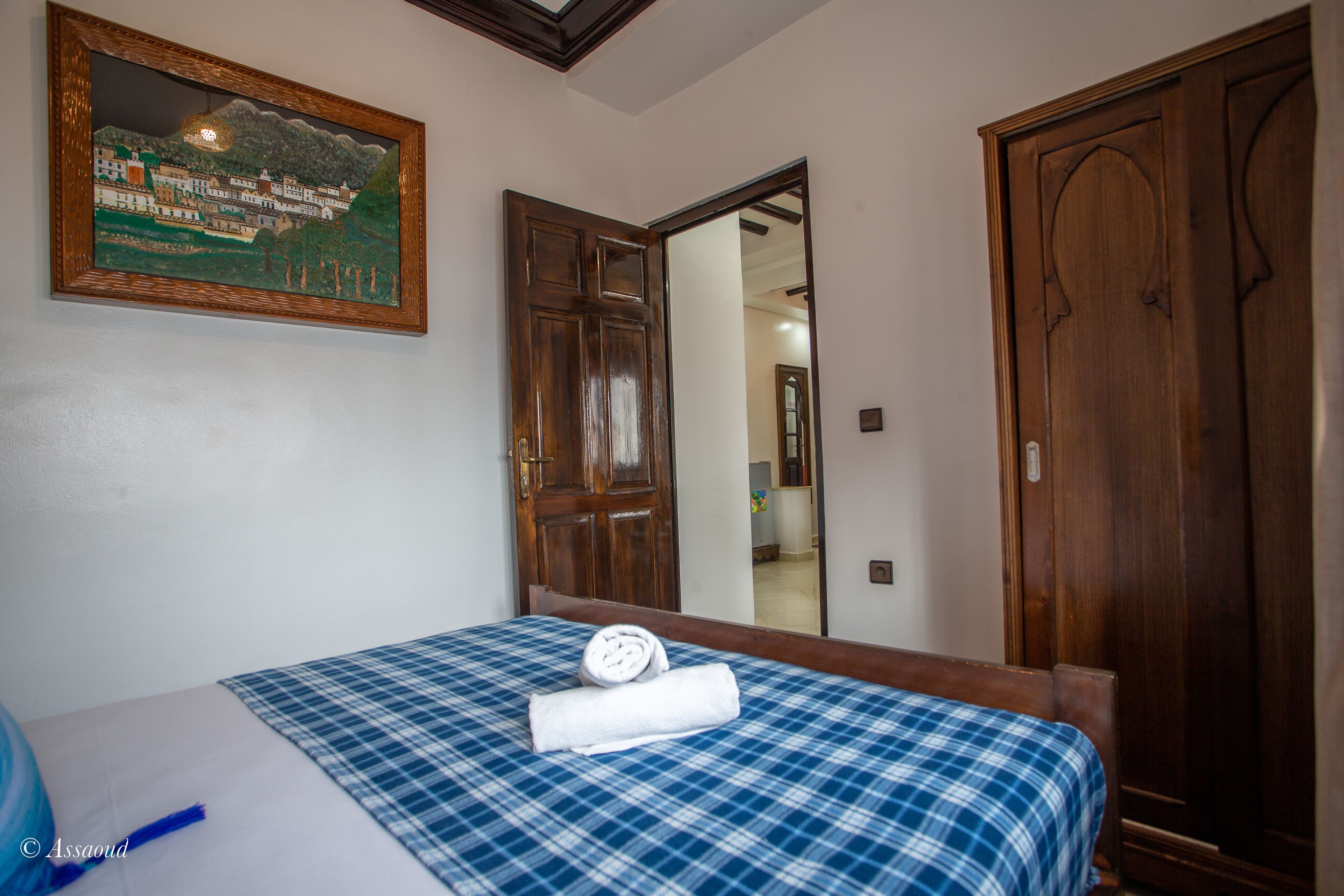 Une chambre d’hôtel avec une couvre-lit à carreaux, un tableau au mur et des portes en bois.