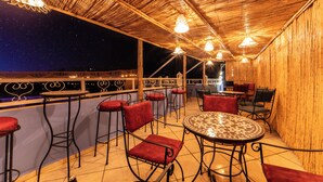 Un espace extérieur aménagé avec des tables et des chaises hautes, une table décorée et une vue sur le ciel nocturne.
