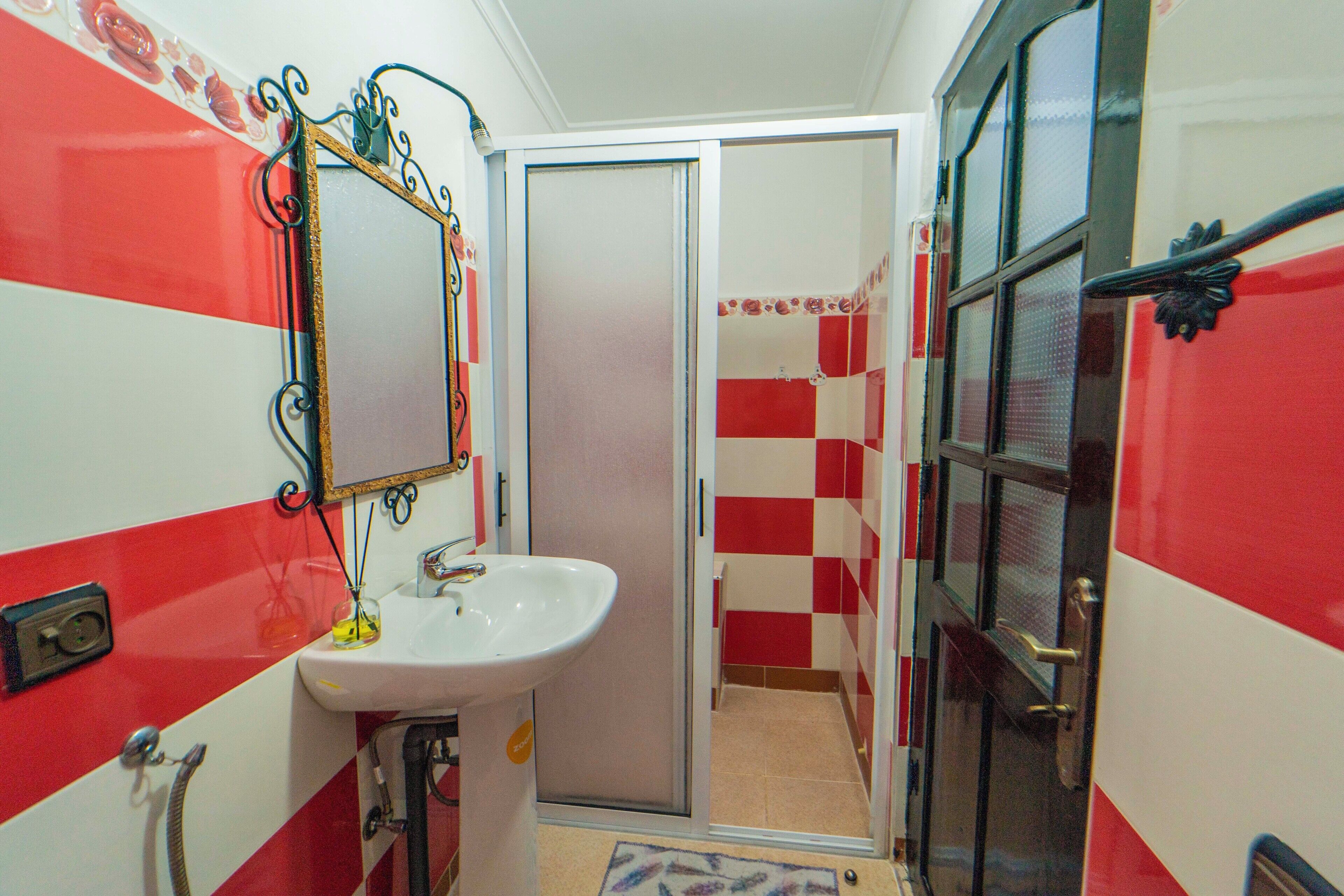 Une salle de bain avec un mur à motifs à carreaux rouges et blancs, un lavabo blanc et un miroir doté d’un cadre décoratif.