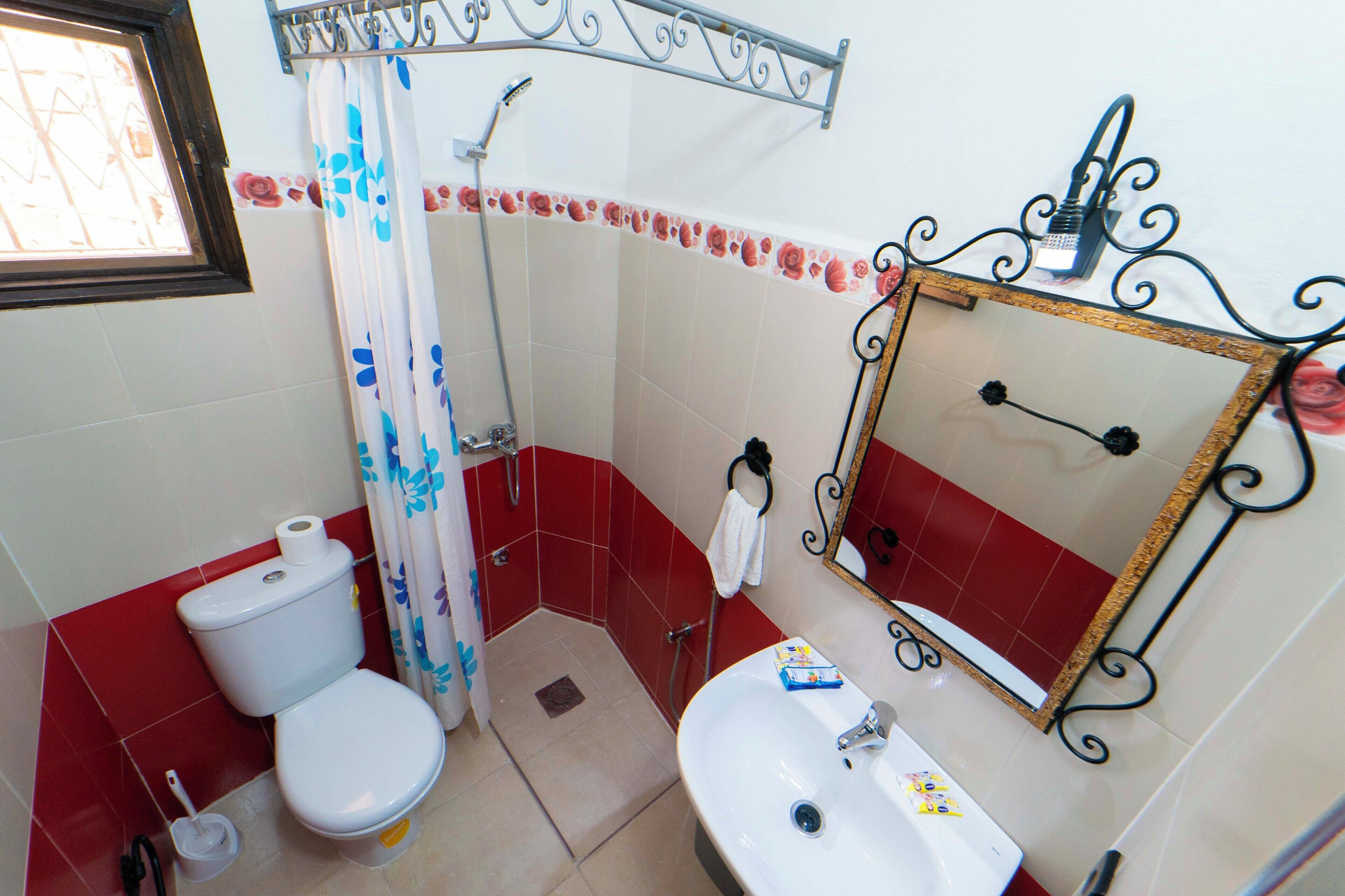 A bathroom with a toilet, sink, shower, and a mirror with a decorative frame.