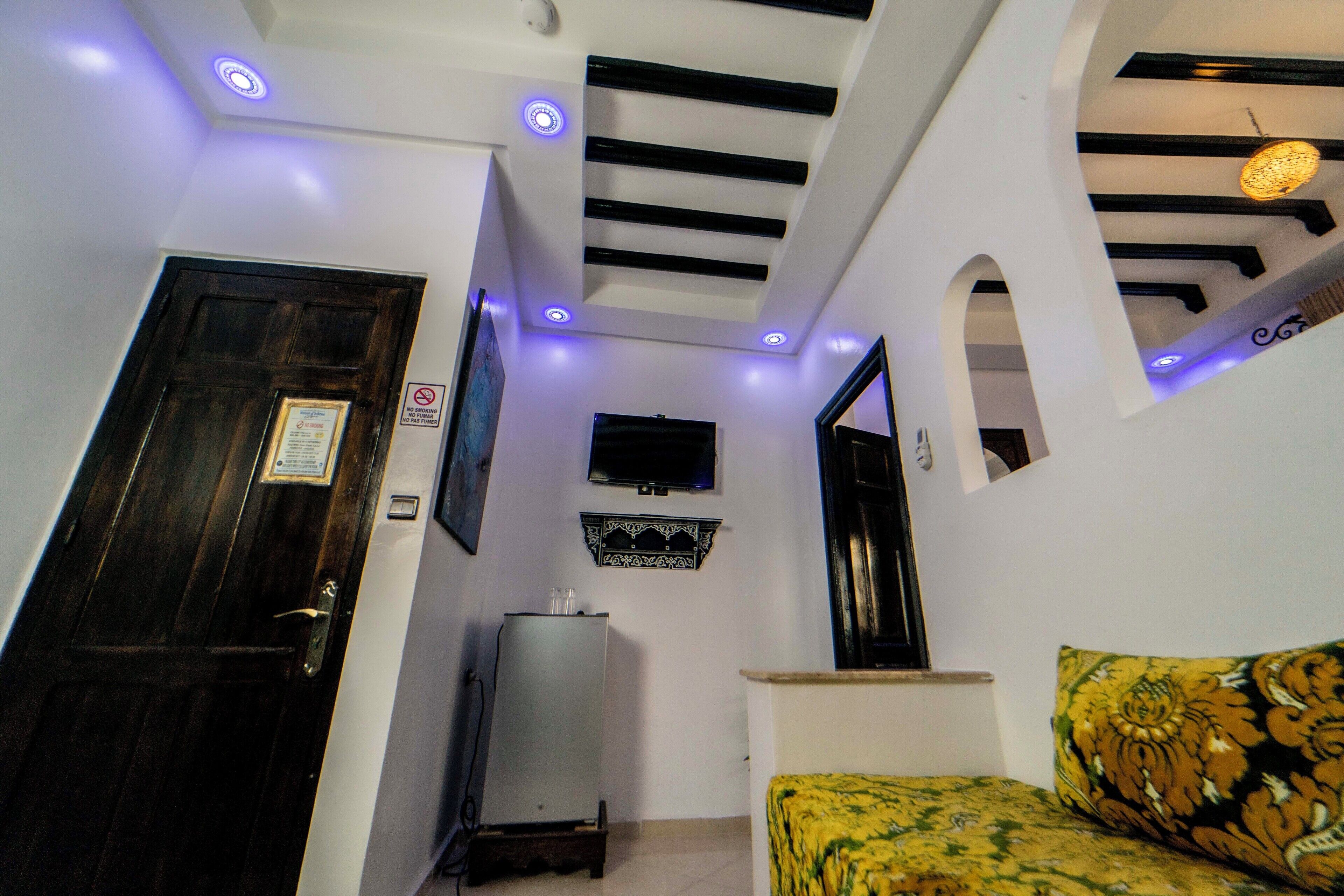 Una habitación con cama, televisor montado en la pared, techo con iluminación empotrada y una puerta con un cartel.