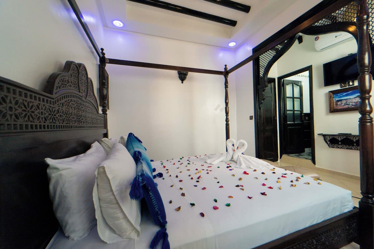 Una cama con dosel cubierta con una colcha blanca y pétalos de flores de colores esparcidos sobre ella.