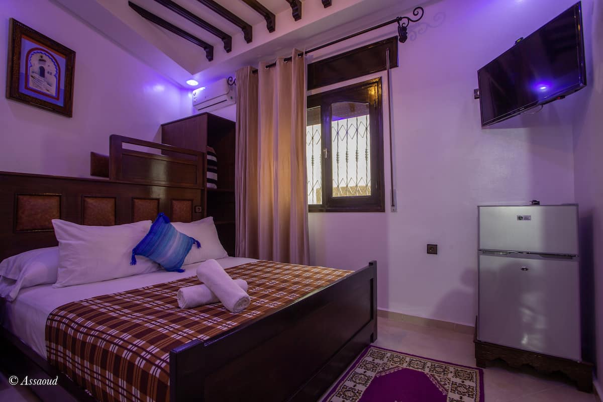Un dormitorio con cama, cortinas, televisor y refrigerador.