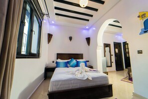 A hotel room with a large bed, a wooden headboard, and a window with curtains. - Maison D'hôtes Afassi (Chefchaouen)