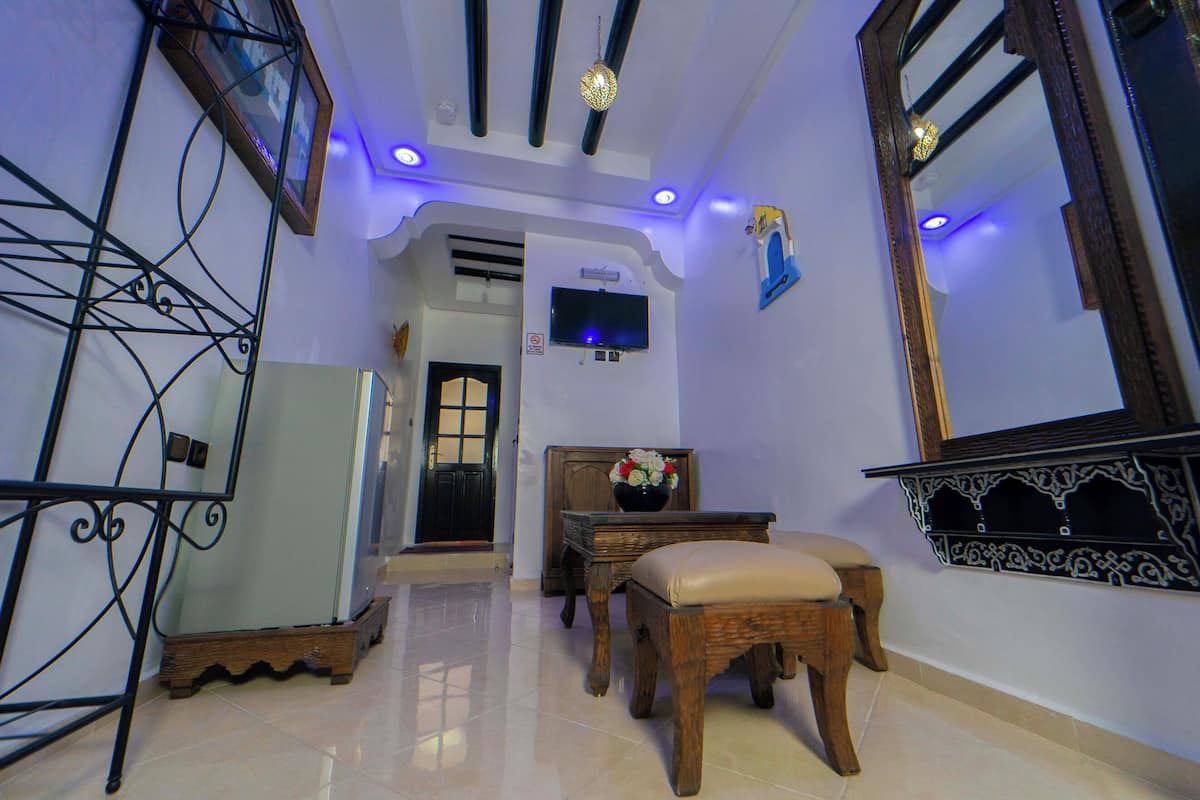 Una habitación con un banco de madera, una mesa pequeña con un florero y un televisor en la pared.