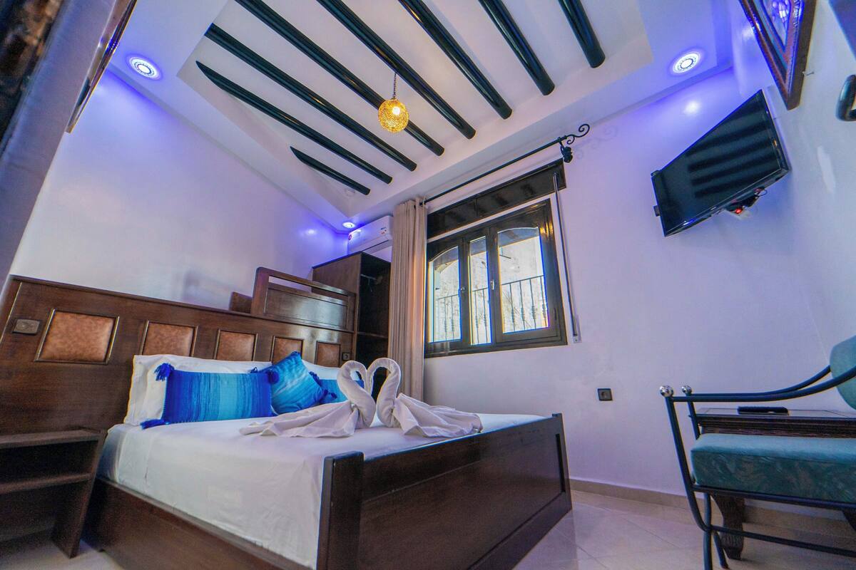 Un dormitorio con cama, una silla, televisión y ventana.