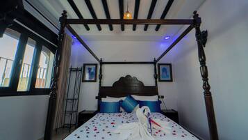 A four-poster bed with a white bedspread and blue pillows, a wooden headboard, and a hanging light fixture.