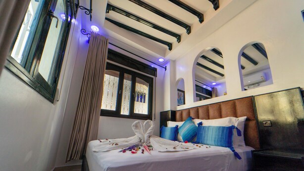 Une chambre d’hôtel avec un lit, une tête de lit, une fenêtre et un rideau.