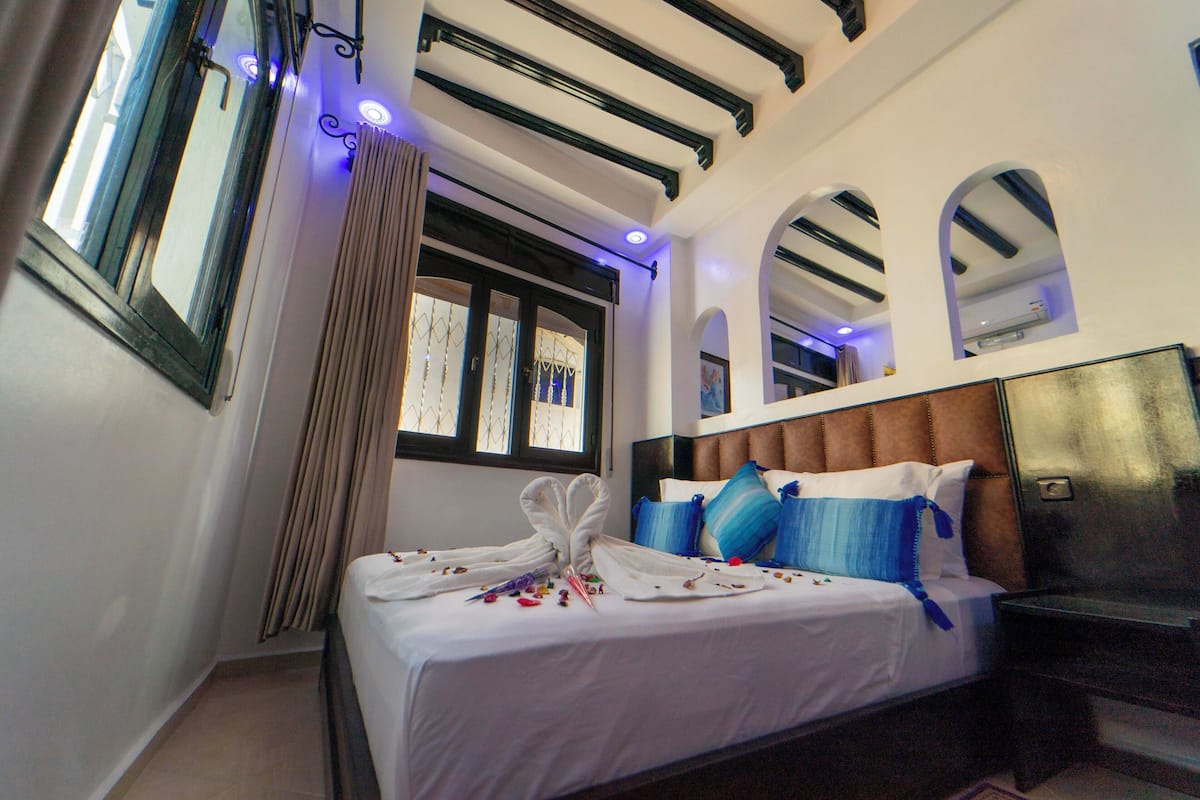 Una habitación de hotel con cama, cabecera, ventana y cortina.