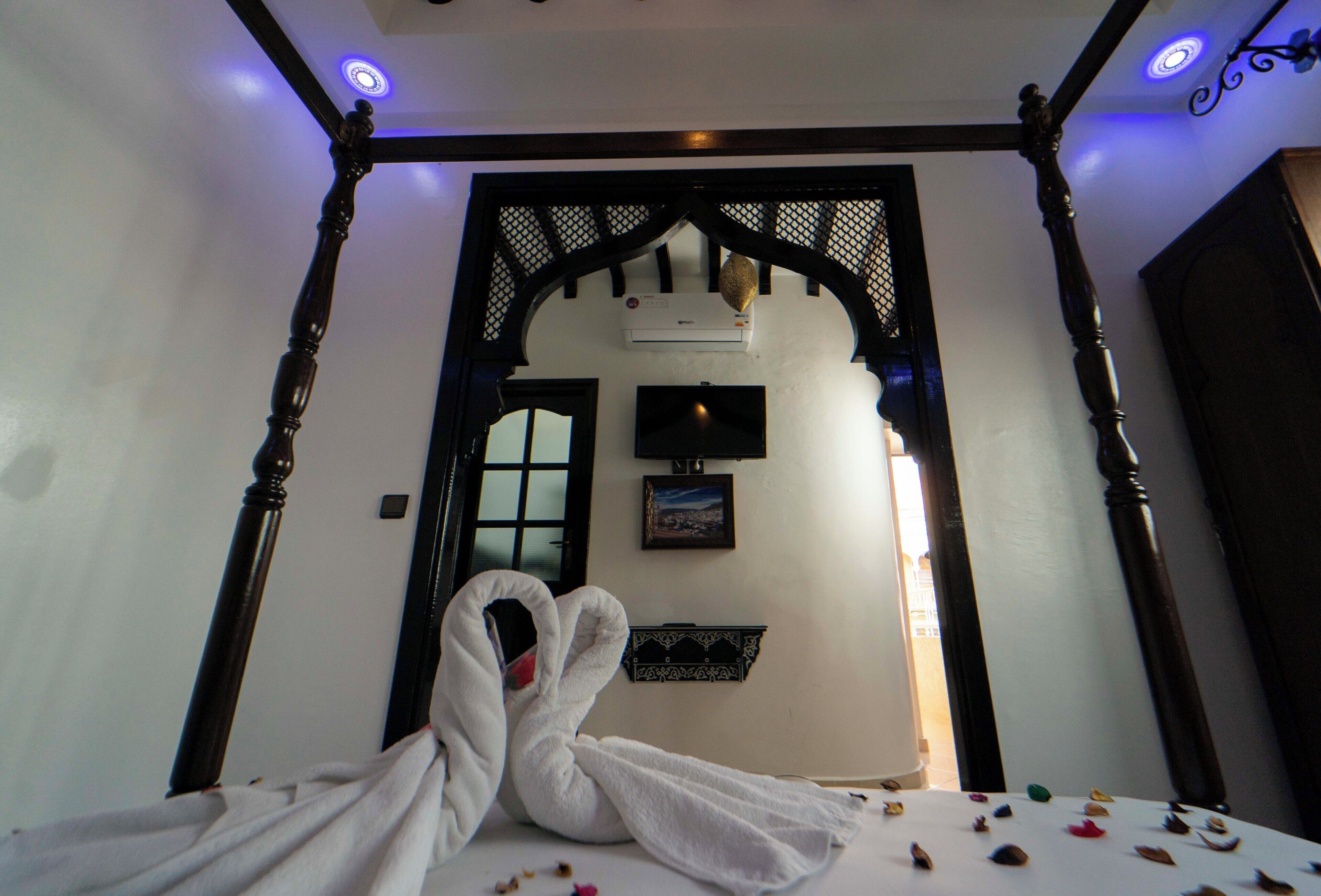 A room with a bed, a wooden canopy, a wall-mounted air conditioner, and a framed picture.