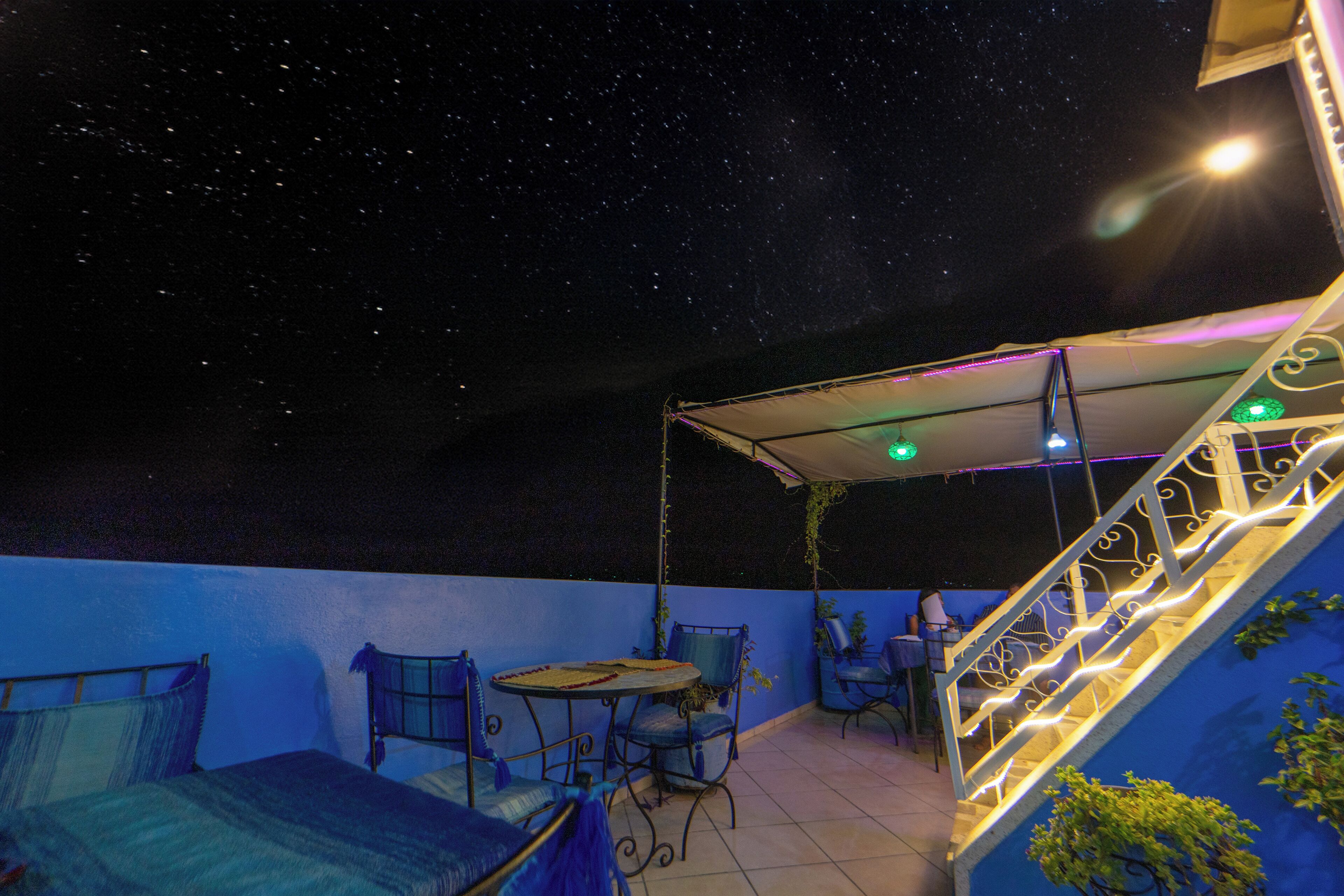 Une terrasse sur le toit dotée d’un espace salon couvert, d’un escalier et d’une vue sur le ciel nocturne.