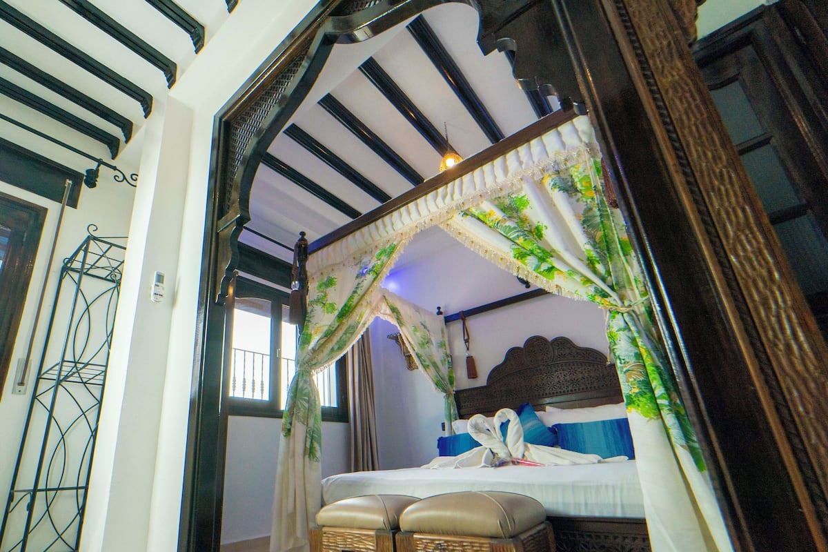 Una habitación con una cama con dosel, un banco de madera y un tapiz estampado.