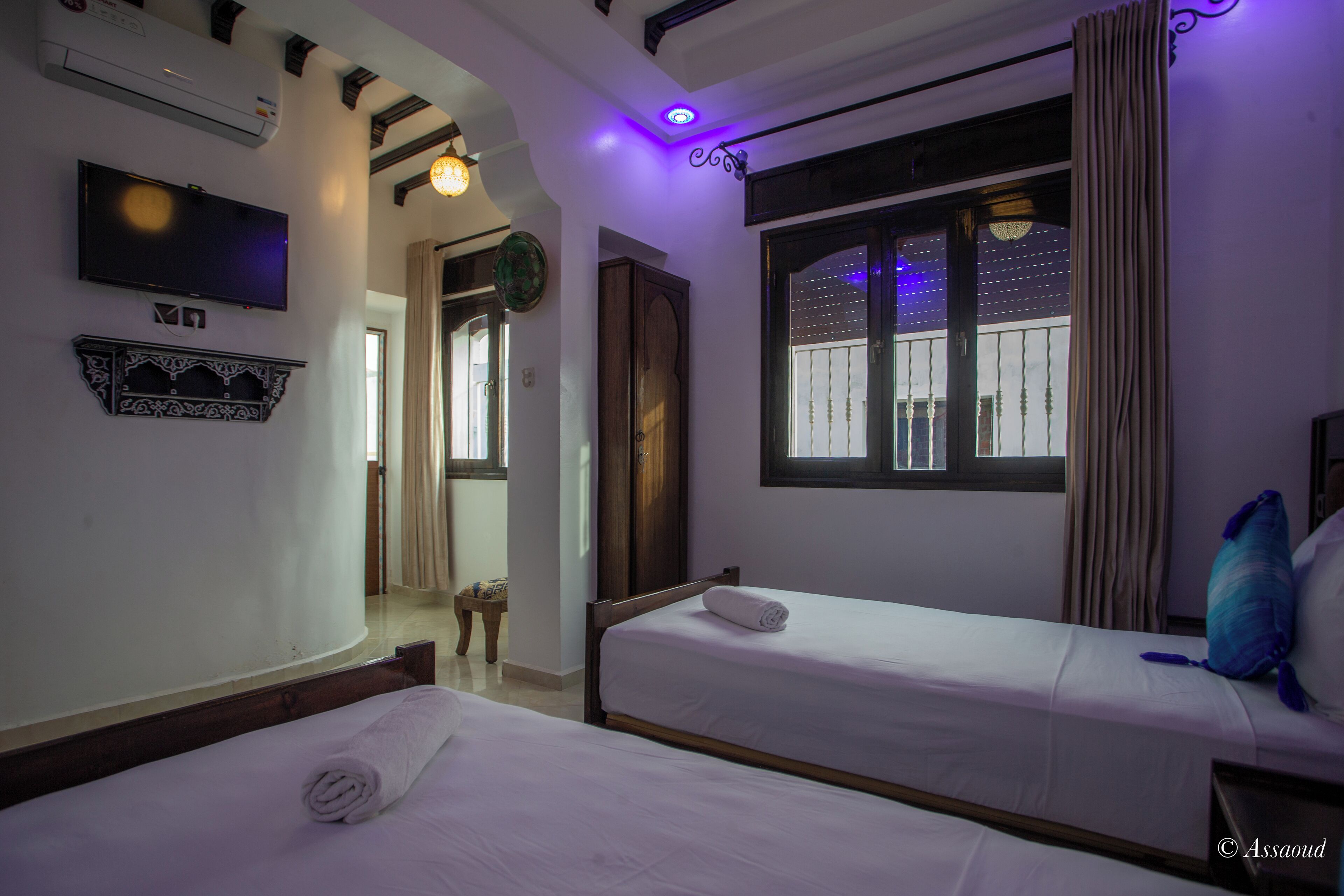 Habitación de hotel con dos camas, televisión y ventana con cortinas.
