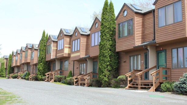 A row of wooden cabins with multiple windows and a central staircase. - Cozy Mountain Condo (Windham)