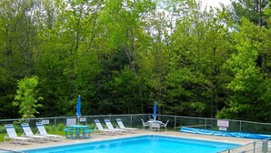 A swimming pool with lounge chairs and tables, surrounded by a fence. Signs indicate no diving allowed and pool hours from 10 AM to 7 PM. - Cozy Mountain Condo (Windham)