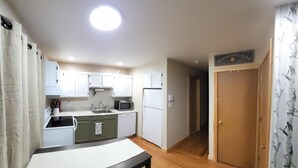 A compact kitchen with white cabinets, a microwave, a sink, and a refrigerator. There is a wooden dining table with chairs. - Cozy Mountain Condo (Windham)