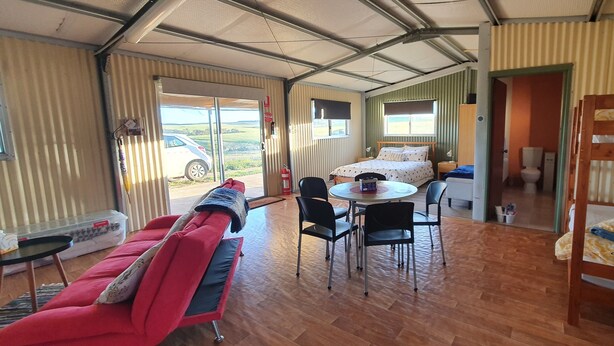 Una habitación con una cama, un sofá rojo, una mesa de comedor con sillas y una cama litera de madera.