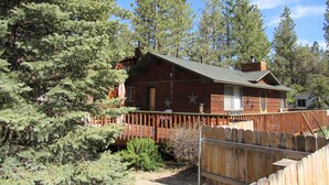 A cabin with a wooden deck, surrounded by dense pine trees.