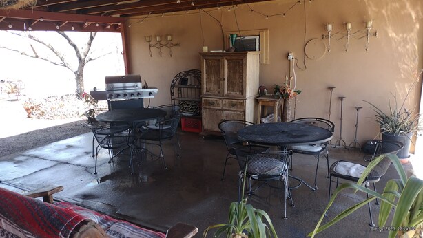 Een terras buiten met metalen tafels en stoelen, een barbecue en een kast.