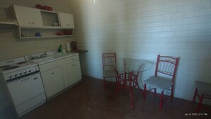 Een compacte keuken met witte kasten, een fornuis en een kleine eettafel met rode stoelen.