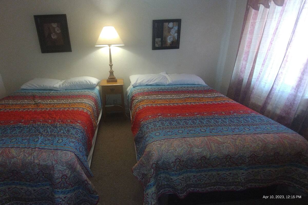 A room with two single beds, a nightstand with a lamp, and two framed pictures on the wall.