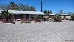 Een motel met een rode gevel, een parkeerplaats met grind en een kleine tuin met cactussen en bloemen.