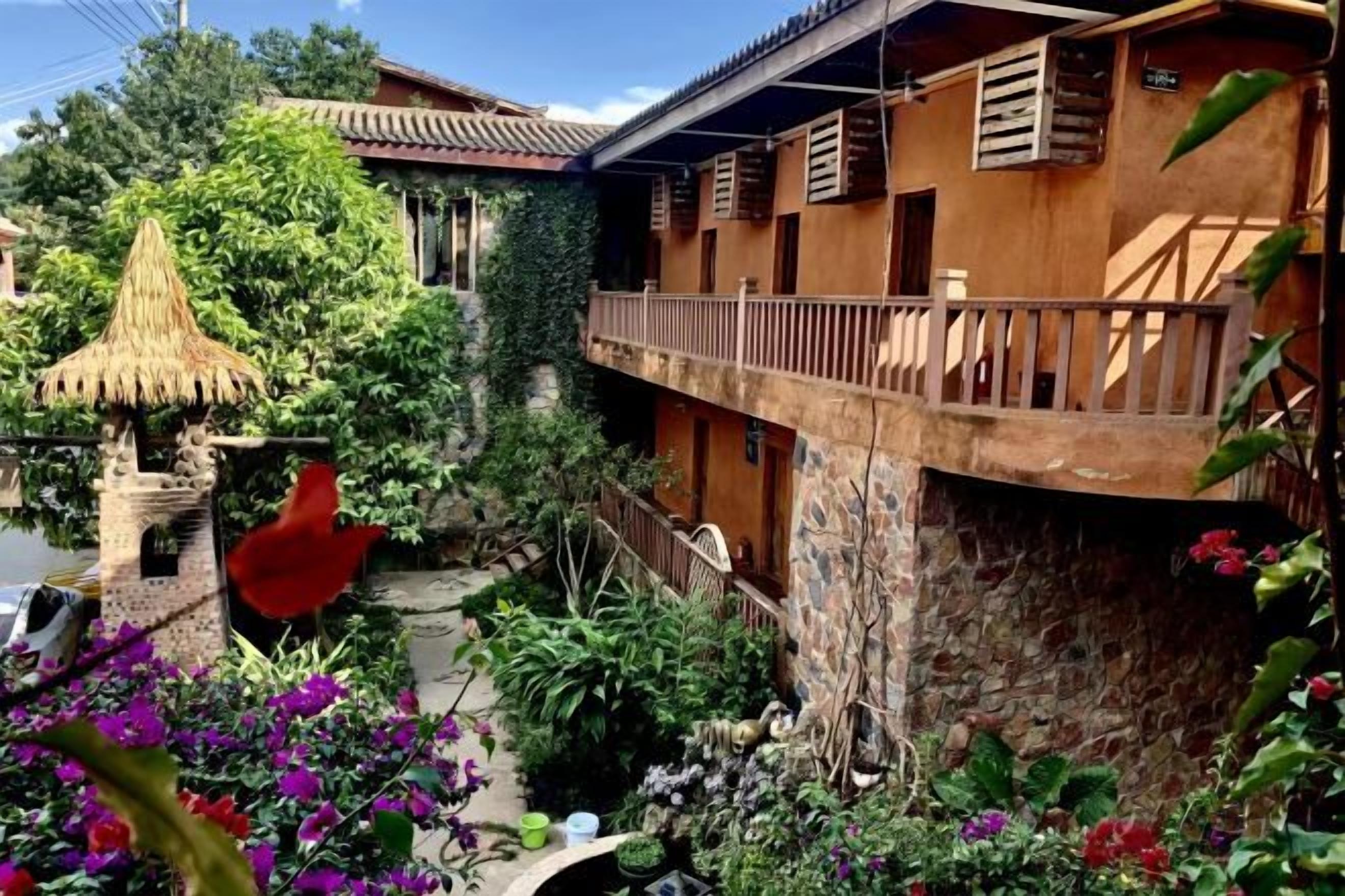 Un patio con una estructura de techo de paja, un muro de piedra y un balcón con barandillas de madera.