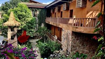 Un patio con una estructura de techo de paja, un muro de piedra y un balcón con barandillas de madera.