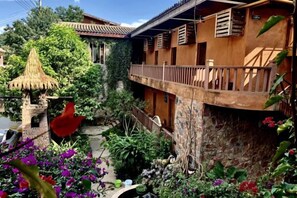 A courtyard with a thatched-roof structure, a stone wall, and a balcony with wooden railings. - Home on the Cloud, Sky Land, Lake View B&B (Qiubei)