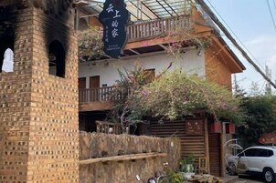 Una casa tradicional japonesa con una chimenea de ladrillo, un balcón con baranda de madera y un coche estacionado en frente.