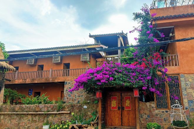 A traditional building with a wooden door and balcony, surrounded by lush greenery and vibrant flowers.