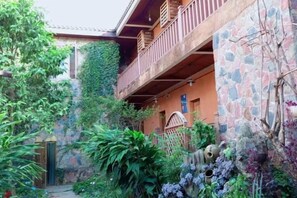 A courtyard with a stone wall, a wooden balcony, and lush greenery. - Home on the Cloud, Sky Land, Lake View B&B (Qiubei)