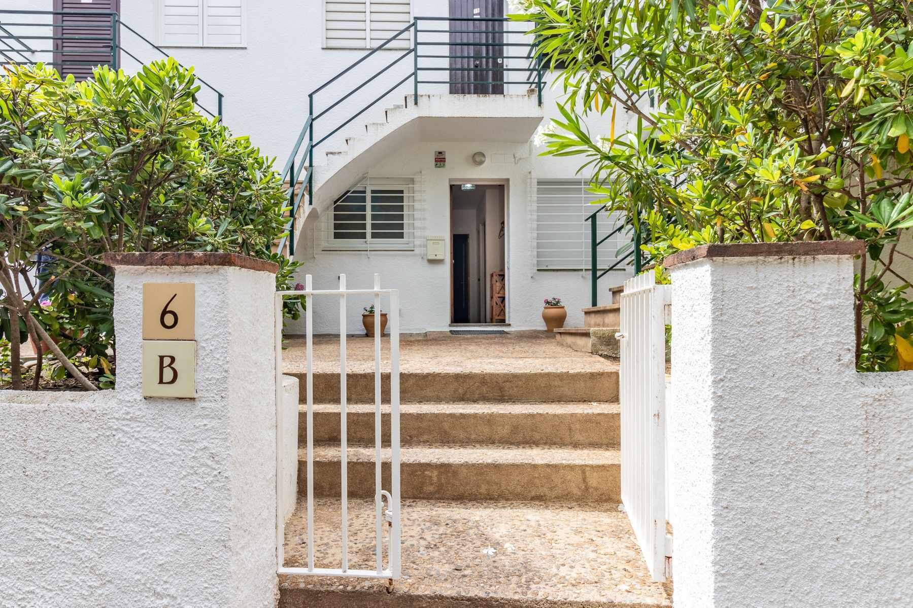 Un bâtiment blanc avec un escalier menant à une porte, le tout entouré de verdure.