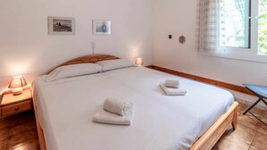 Una cama bien hecha con dos almohadas, una mesita de noche con una lámpara y dos cuadros enmarcados en la pared.