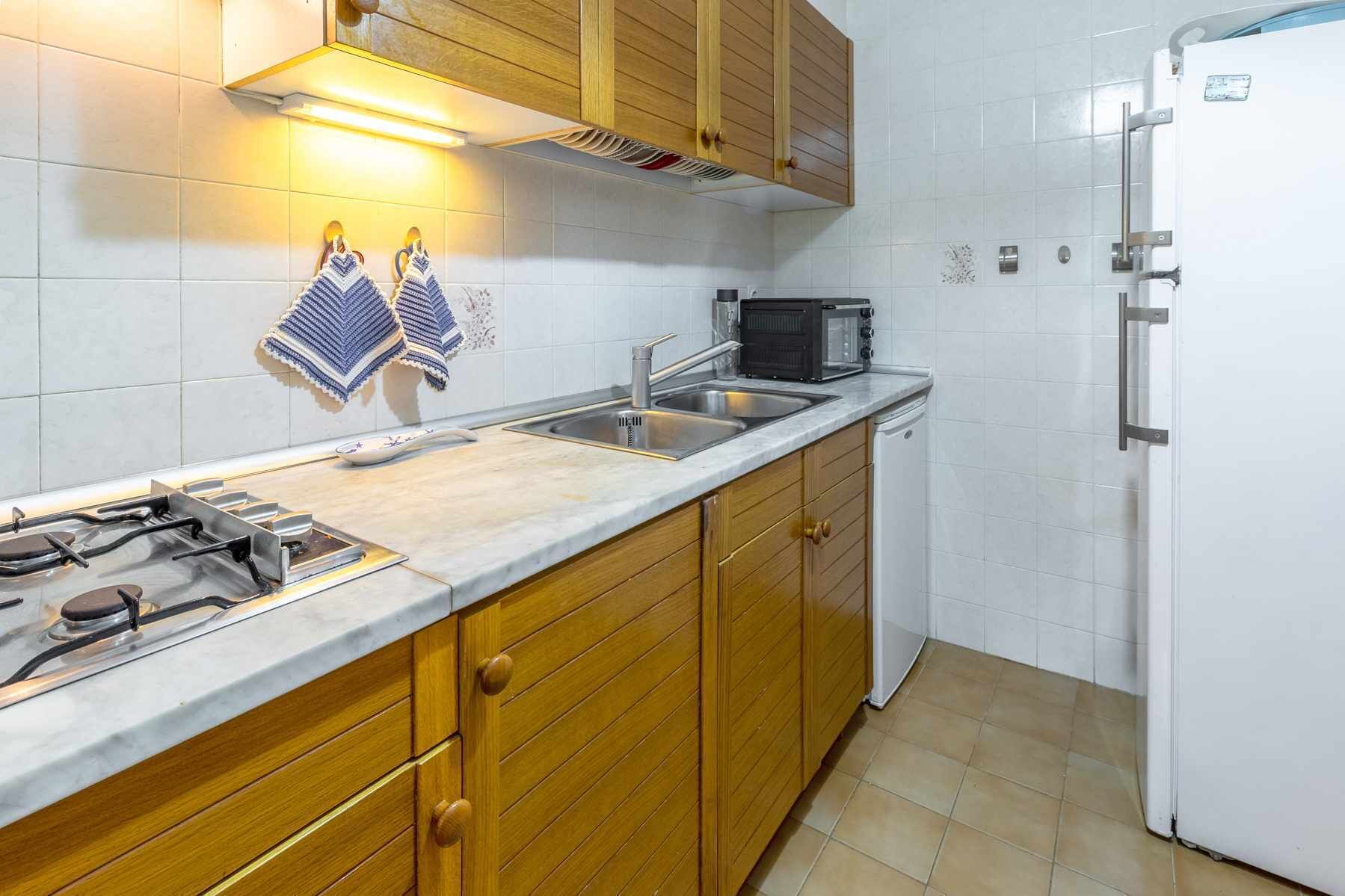 Eine Küche mit Holzschränken, einem weißen Kühlschrank, einer Mikrowelle, einem Gasherd und einem Spülbecken.