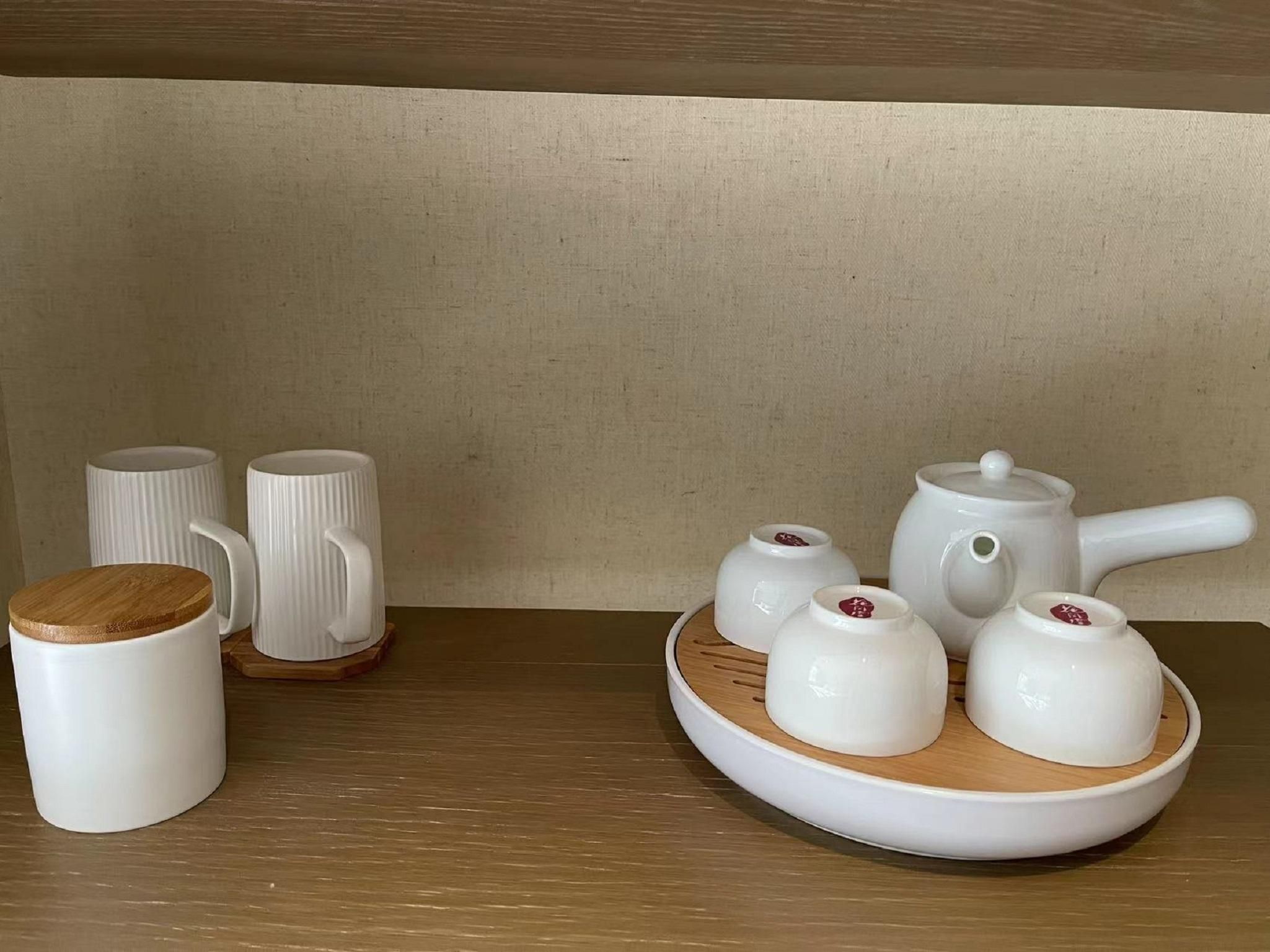 A tea set with a teapot, cups, and a wooden tray on a wooden table against a plain wall.