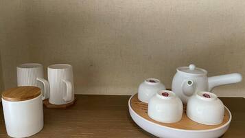 A tea set with a teapot, cups, and a wooden tray on a wooden table against a plain wall.