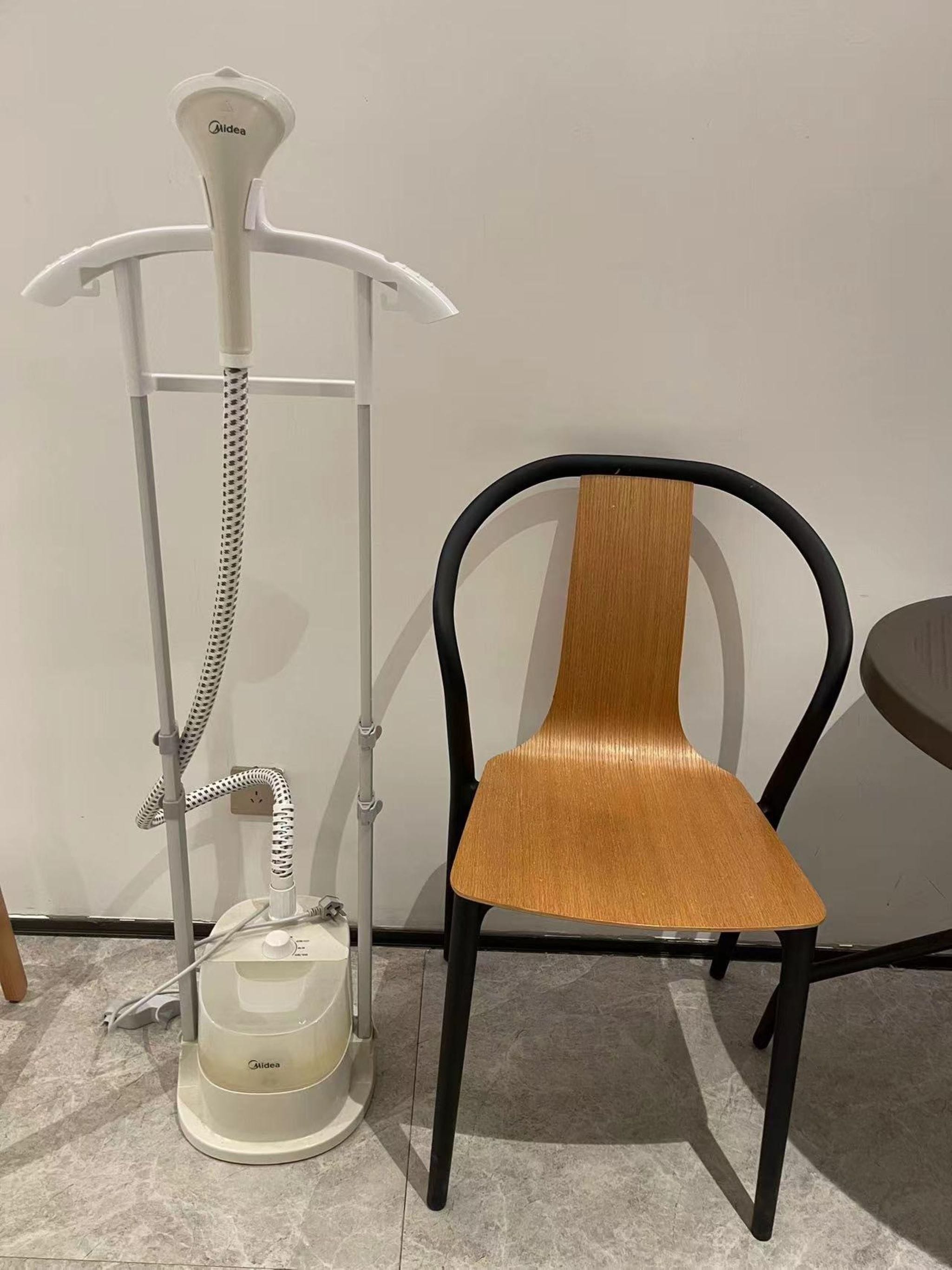 Una lámpara de pie blanca con cuello flexible y una base identificada con el nombre 'Aidea', junto a una silla de madera con patas de metal negro.